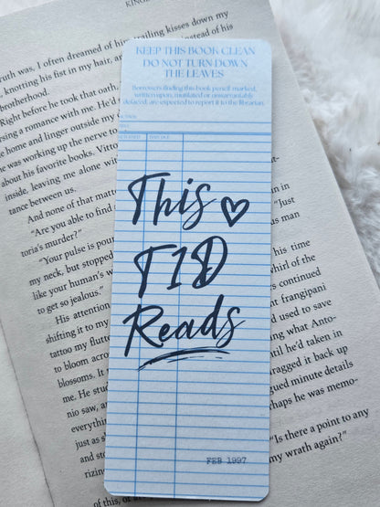 A blue lined bookmark with handwritten text reading 'This is T1D Reads' placed on top of printed book pages.