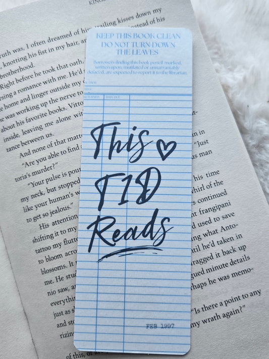A blue lined bookmark with handwritten text reading 'This is T1D Reads' placed on top of printed book pages.
